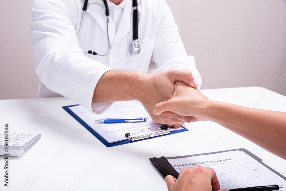 Female And Male Doctor Sitting At Desk Shaking Hands