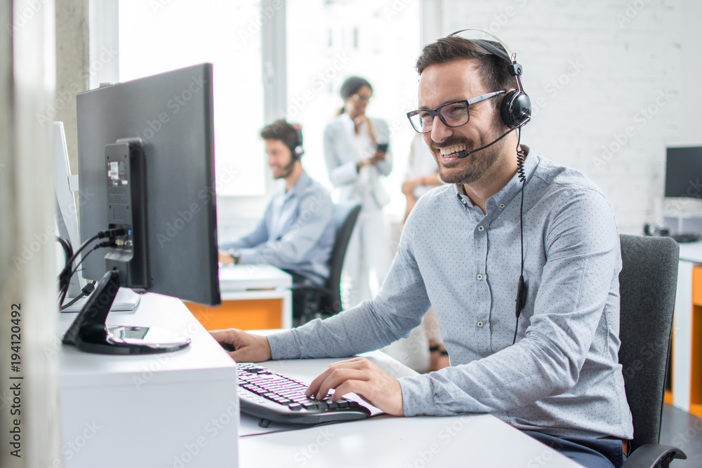 Smiling customer support operator with hands-free headset working in the office.